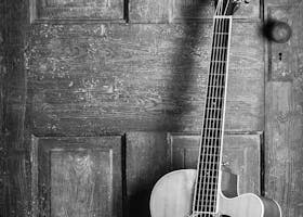 A classic acoustic guitar leaning against a rustic wooden door in a black and white vintage style.