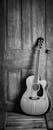 A classic acoustic guitar leaning against a rustic wooden door in a black and white vintage style.