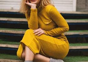 Stylish woman in yellow dress and sunglasses posing on steps. Modern fashion portrait.