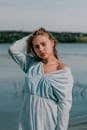 A fashionable woman poses gracefully in a light blue dress by a tranquil lake, embodying elegance.