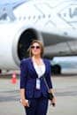Stylish businesswoman standing confidently in front of an airplane at an airport, exuding professionalism.