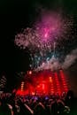 Energetic outdoor concert at night with a vibrant fireworks display and crowd enjoying live music.