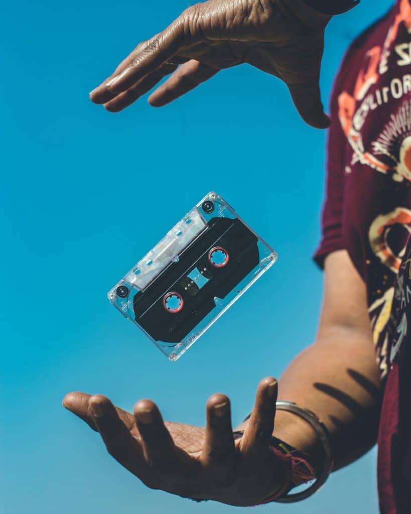 A retro cassette tape floating between hands against a clear blue sky, evoking nostalgia.