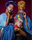 Three women in colorful African outfits with face paint and headdresses celebrating culture.