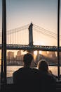 A romantic couple watches the sunset behind the iconic Manhattan Bridge in New York City.