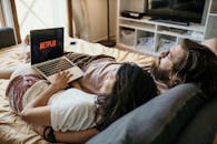 A cozy couple lounging in bed, streaming Netflix together on a laptop, enjoying a peaceful moment.