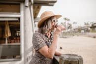 Stylish woman in leopard print and hat enjoying coffee outside a cafe by the beach.