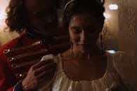 A couple dressed in vintage attire sharing an intimate moment indoors, low light.