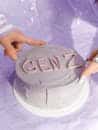 A minimalist purple cake with 'GEN Z' icing, touched by hands.