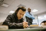 College student writing exam under supervision in a classroom.