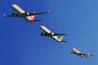 Three commercial airplanes soaring through a clear blue sky, highlighting aviation technology.