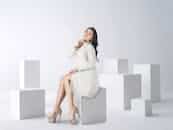 Elegant Asian woman in a fashionable white coat posing in a modern studio setting.