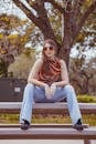 Chic young woman with sunglasses sitting on a park bench in Tampa, exuding a playful and relaxed vibe.