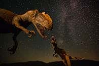 Silhouetted dinosaur statues under a vivid Milky Way night sky.