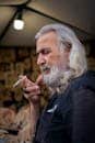 Portrait of an elderly man with long grey hair smoking a cigarette indoors.