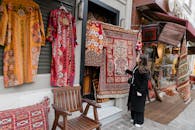 Woman exploring traditional embroidered carpets and tunics at an outdoor shop's entrance.