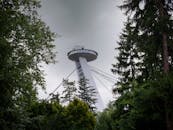 View of the UFO Tower in Bratislava, Slovakia through lush greenery on a cloudy day.