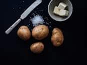 High contrast image of potatoes, butter, and salt on a dark background.