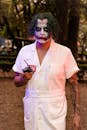 Person in Joker costume and makeup holding a detonator outdoors.