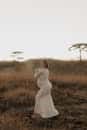 A woman in a white dress stands gracefully in a tranquil field during sunset, exuding elegance.