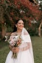 Beautiful bride smiling with floral bouquet during outdoor wedding ceremony.