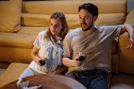 Couple relaxing on sofa enjoying wine at home. Warm, intimate setting perfect for unwinding.
