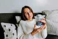 A woman in a cozy sweater holding a snow globe indoors, enjoying a moment of relaxation.