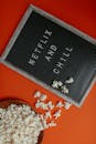 Letter board with 'Netflix and Chill' and popcorn on an orange background, perfect for movie night themes.