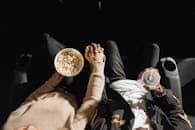 Top view of a couple holding hands in a movie theater with popcorn and drinks.
