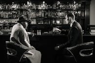 A cinematic, noir-style meeting in a dimly lit bar with a tense atmosphere.