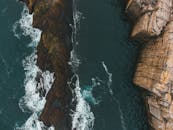 Drone view of dramatic rock formations and crashing waves on a rugged coastline.