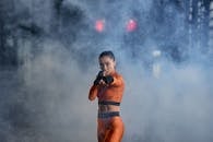 A fierce female cosplayer in an orange costume striking a dynamic pose amidst dramatic smoke.