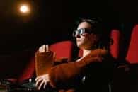 A woman watching a 3D movie in a theater, wearing glasses and holding popcorn.