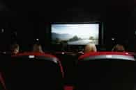 View from behind of people watching a movie in a cinema with red seats and a large screen.
