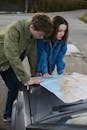 A young couple studies a map on their car hood, planning a road trip adventure.