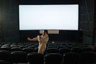 Man standing in an empty movie theater with a blank screen, indoors setting.