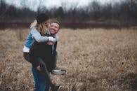 A happy couple enjoys a playful moment in a field during the day, symbolizing love and joy.