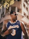 Young man wearing sunglasses and a Lakers jersey posing in urban outdoors.
