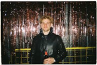 A young man in a black leather jacket smiling and holding a beer bottle in front of festive tinsel. Perfect for party and nightlife themes.