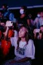 A teenager captures a live concert using her smartphone, surrounded by an audience.