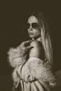 Stylish woman in fur coat and sunglasses posing confidently in a modern fashion portrait.