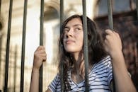 A teenage girl looks thoughtfully through bars, symbolizing hope and freedom.