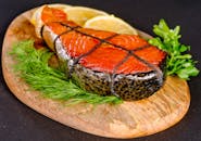 Delicious grilled salmon steak served with fresh herbs and lemon slices on a wooden board.