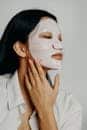 An Asian woman gently applies a face mask as part of her skincare routine, focusing on beauty and self-care.