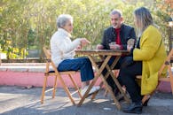 Three senior friends playing a card game outdoors, enjoying leisure time together.