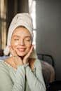 A smiling woman with under-eye patches and towel on head, embracing self-care.