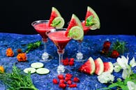 Close-up of vibrant watermelon and lime cocktails garnished with flowers on a studio setup.