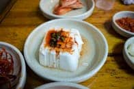 Elevated shot of tofu garnished with sauce and vegetables, surrounded by Korean side dishes.