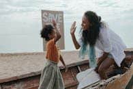 Mother and child high-five during a fun beach cleanup with a save the planet sign.
