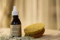 A close-up of a natural bath setup featuring a wooden brush and essential oil bottle.